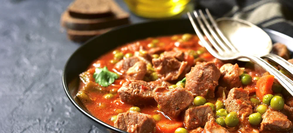 Veal stewed with vegetables in tomato sauce on a black concrete or stone background.