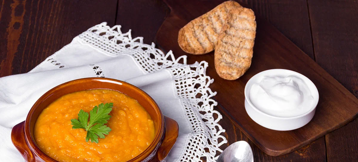 Pumpkin soup on wooden table served with greek yougurt and wheat rusks.