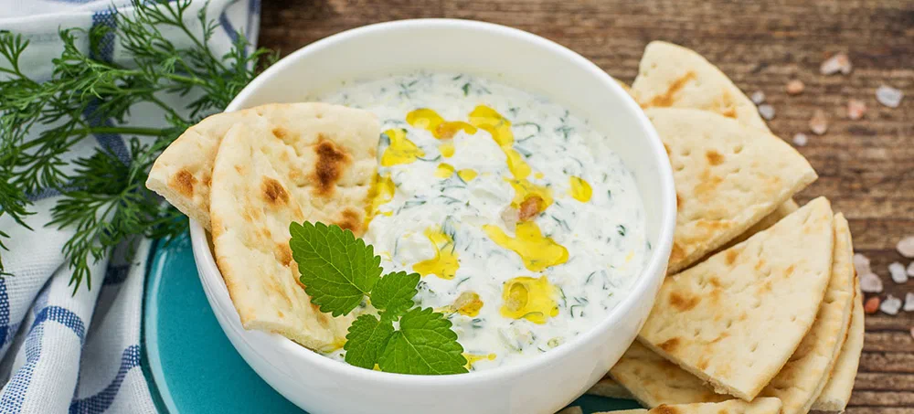 Sauce with yogurt and cucumber for starter with slices of bread on a white plate and a dark natural wood background. selective Focus